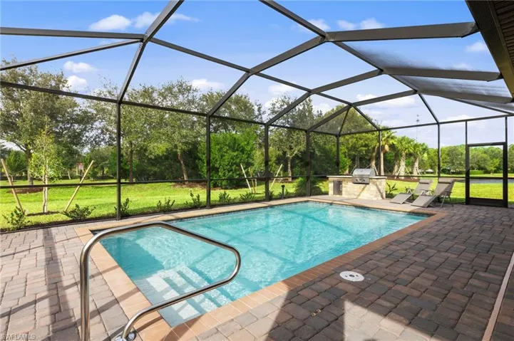 Screened-in pool area featuring a rectangular pool with integrated steps, stainless steel handrail, and paver decking