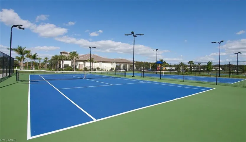 Multiple hard-surface tennis courts featuring blue playing areas and green surrounds