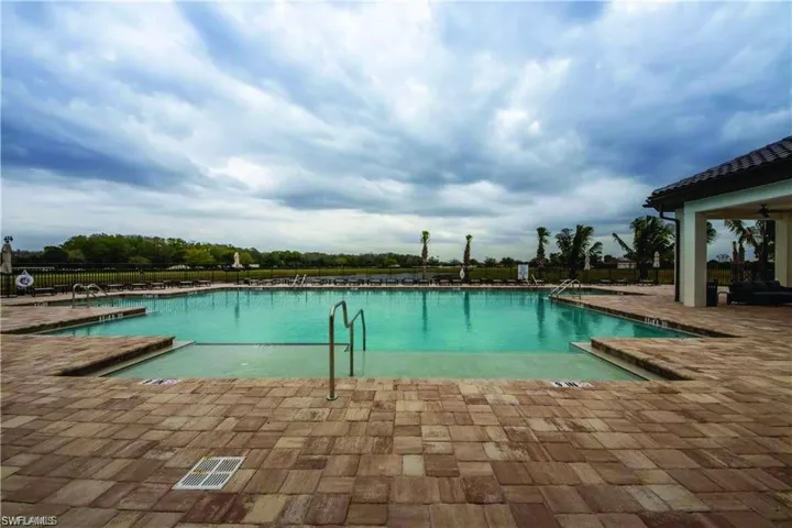 Expansive outdoor pool with integrated shallow entry and handrails, surrounded by a paver patio