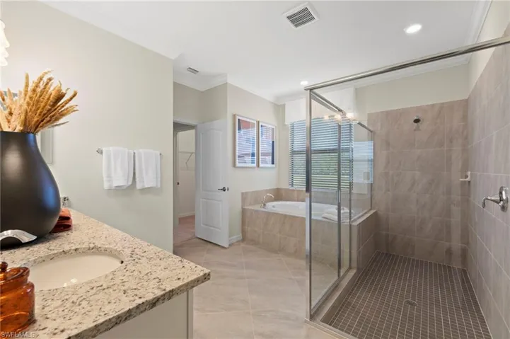 Spacious bathroom featuring a large walk-in shower with glass enclosure, a jetted soaking tub, a single vanity with granite-finish countertop, tiled flooring, and recessed lighting