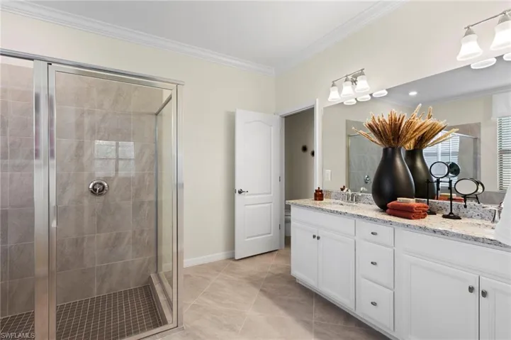 Bright bathroom featuring a glass-enclosed shower with tiled walls and floor, a dual vanity with a light-colored countertop, white cabinetry, and a large mirror