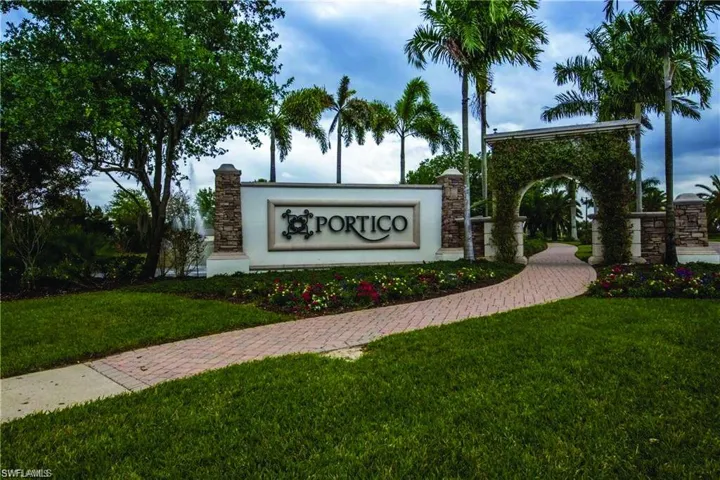 Community entrance featuring a stone-clad monument sign with raised lettering, an arched trellis covered in greenery, mature palm trees, and a paved walkway