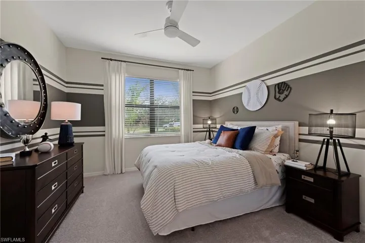 Carpeted bedroom featuring a window with horizontal blinds, a ceiling fan, and a neutral color palette with accent stripes