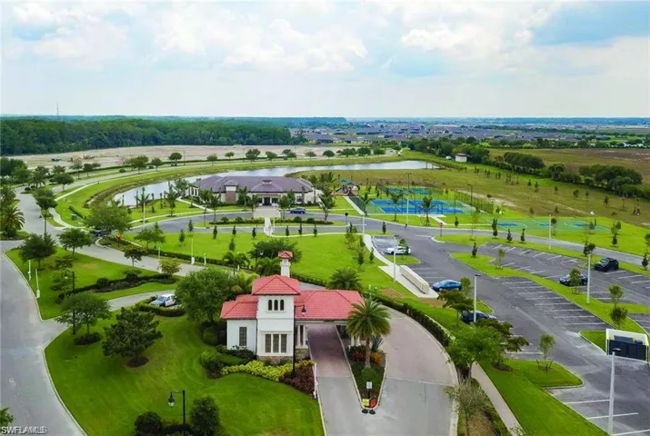Gated community entrance featuring Mediterranean-inspired architecture, manicured landscaping, a private lake, clubhouse, and tennis courts