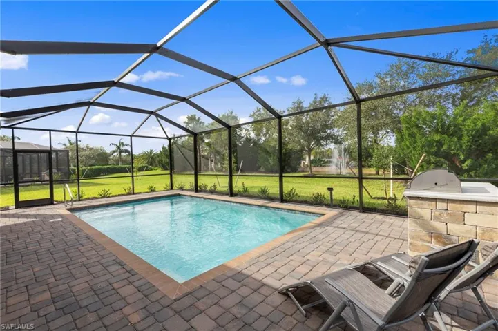 Screened pool enclosure featuring a rectangular pool with integrated steps, paver decking, and a built-in outdoor cooking station with a stone facade