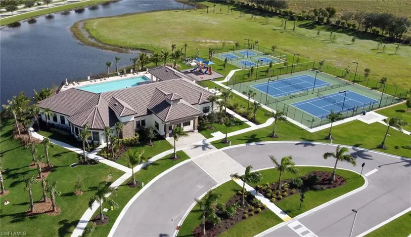Community clubhouse featuring a rectangular swimming pool, multiple tennis courts, pickleball courts, and a playground, all surrounded by manicured lawns and mature palm trees