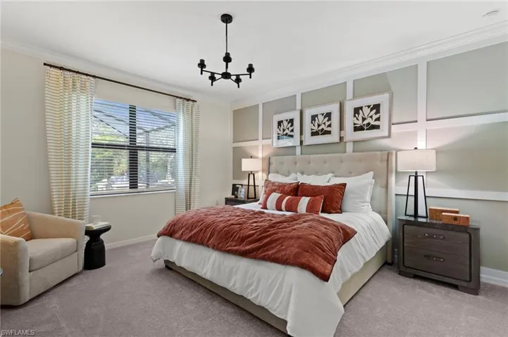Bedroom featuring a large window, plush carpet flooring, a decorative wall panel accent, and a contemporary black chandelier