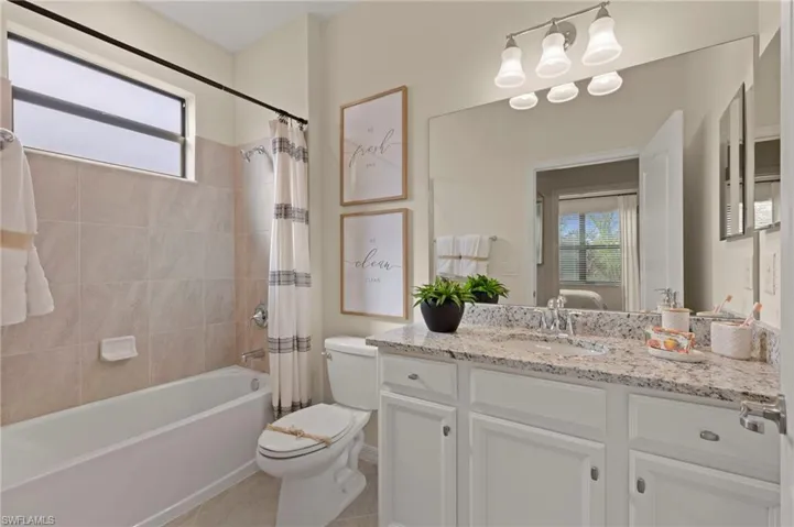 Bathroom featuring a tub/shower combination with beige tile surround, white vanity with a granite-style countertop, integrated sink, and an expansive mirror