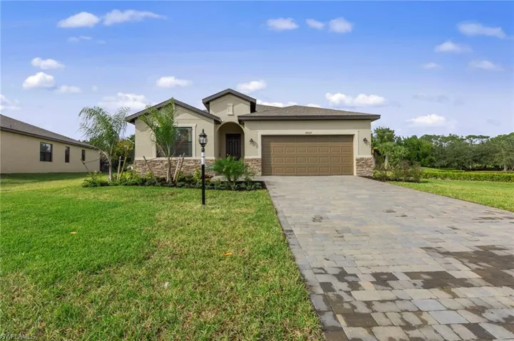 Stucco exterior with stone accenting, a paver driveway, an attached garage, and mature landscaping