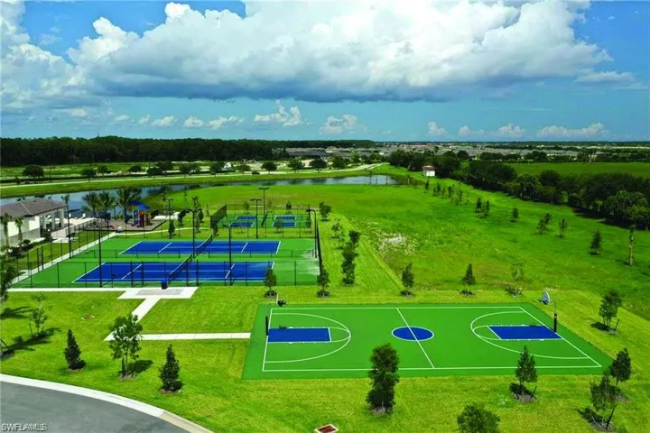 Expansive recreational area featuring multiple pickleball courts, a full basketball court, a playground structure, and a large body of water