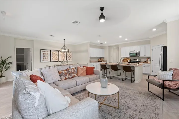 Open-concept living area featuring light-toned flooring, crown molding, and recessed lighting