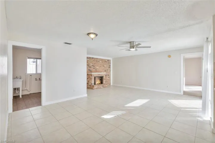 Unfurnished living room featuring ceiling fan, a textured ceiling, a brick fireplace, and light tile patterned floors
