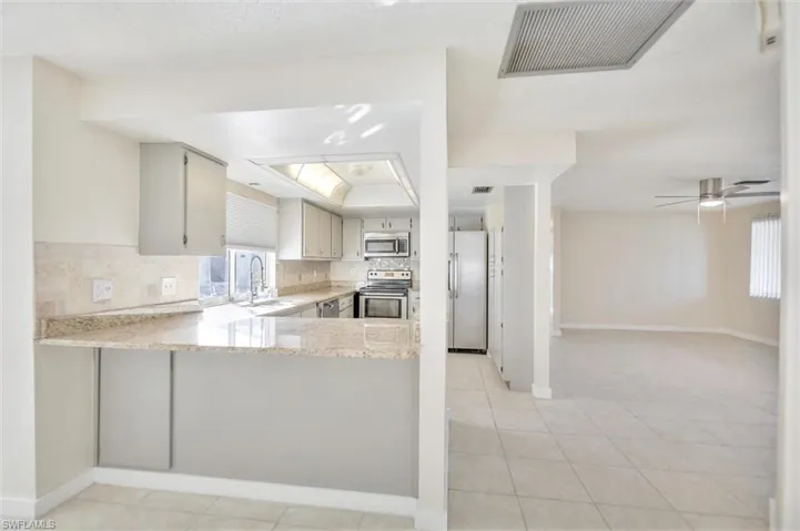 Kitchen with backsplash, stainless steel appliances, ceiling fan, a peninsula, and light stone counters