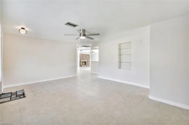 Empty room featuring built in features, a stone fireplace, ceiling fan, and light tile patterned floors