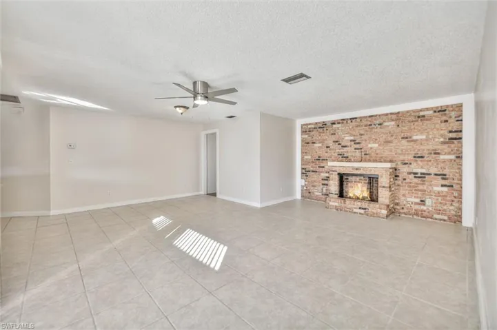 Unfurnished living room with brick wall, a fireplace, a ceiling fan, a textured ceiling, and light tile patterned floors