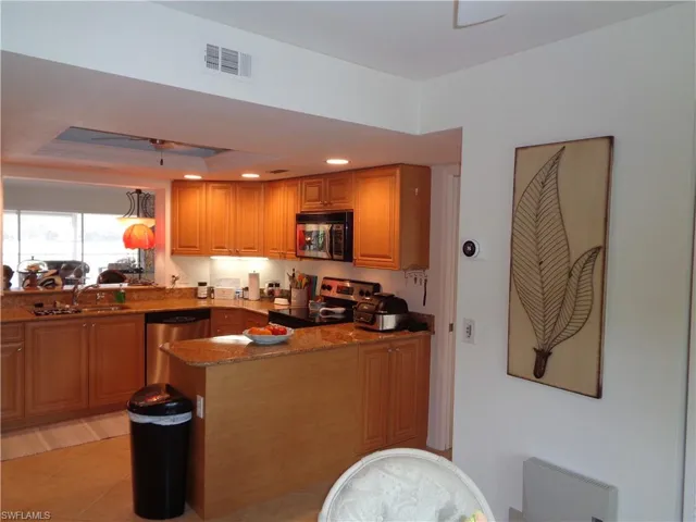 Kitchen featuring a peninsula, stainless steel appliances, stone countertops, recessed lighting, and a raised ceiling