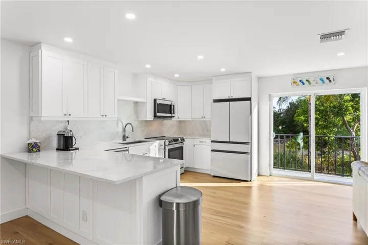 Kitchen featuring white cabinets, stainless steel appliances, a peninsula, light stone counters, and light wood-style flooring