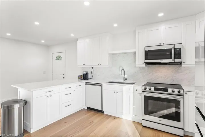 Kitchen with stainless steel appliances, white cabinetry, a peninsula, recessed lighting, and light wood-type flooring