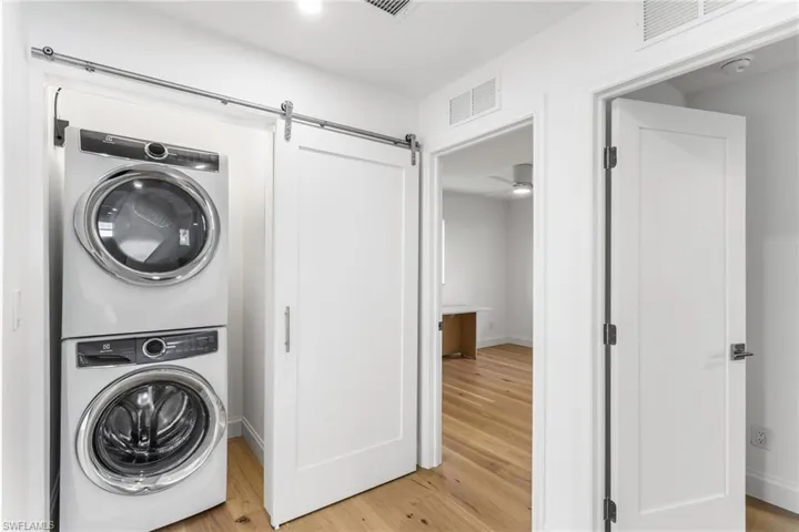 Laundry area featuring light wood-type flooring, stacked washer and clothes dryer, a barn door, and a ceiling fan