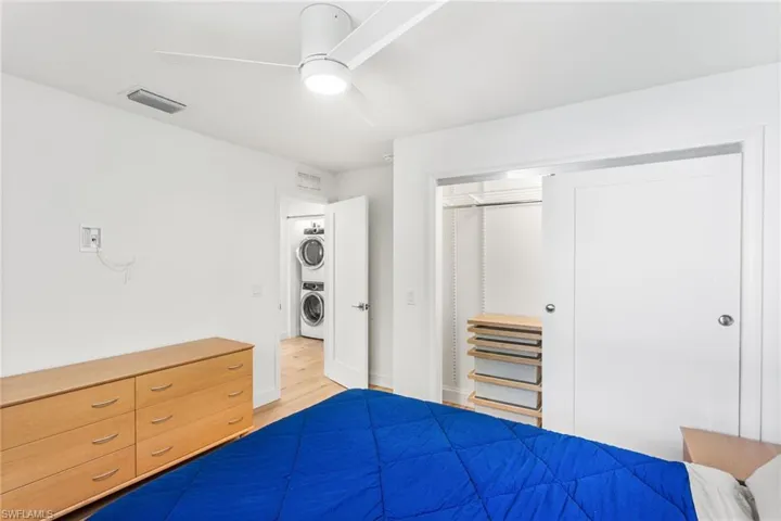 Unfurnished bedroom featuring a closet, ceiling fan, stacked washer and clothes dryer, and light wood finished floors