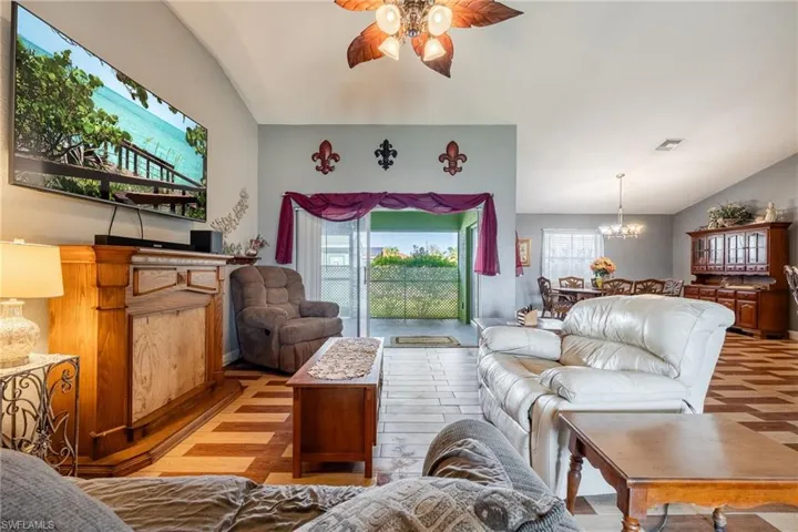 Living room with ceiling fan with notable chandelier, light wood-type flooring, and lofted ceiling