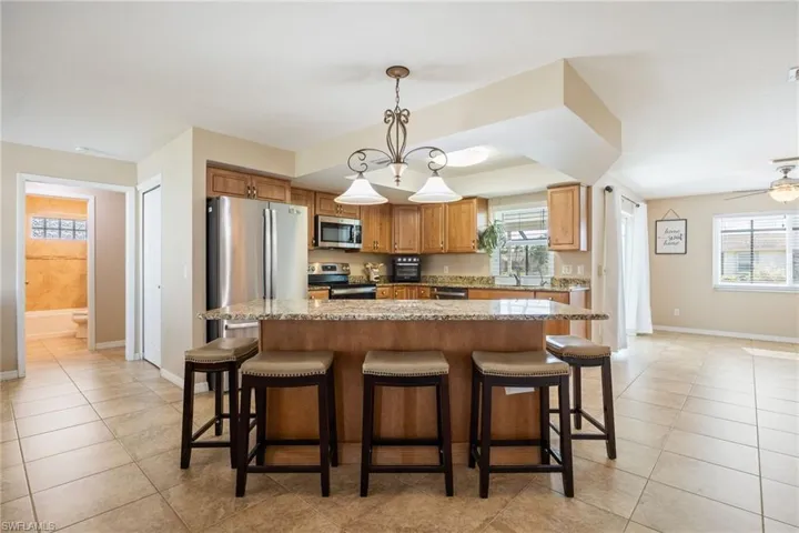 Kitchen featuring decorative light fixtures, a breakfast bar area, light stone countertops, and appliances with stainless steel finishes