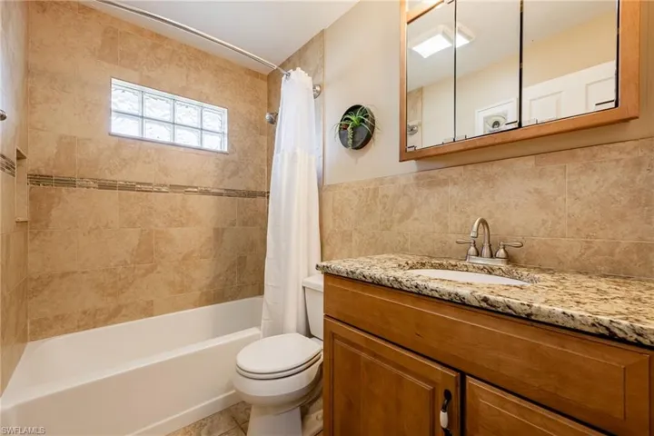 Full bathroom with vanity, shower / tub combo with curtain, tile walls, and light tile patterned floors