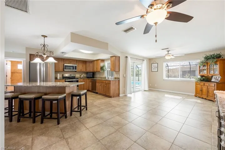 Kitchen featuring decorative light fixtures, a kitchen bar, brown cabinets, stainless steel appliances, and light stone counters