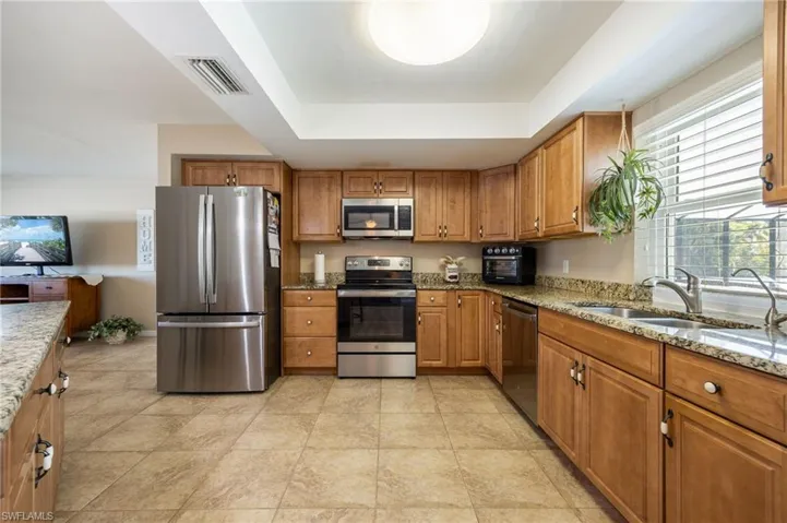 Kitchen with light stone counters, appliances with stainless steel finishes, and brown cabinets