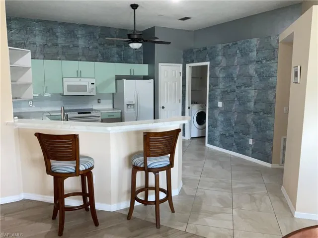 Kitchen with a kitchen bar, white appliances, light countertops, a peninsula, and tile walls