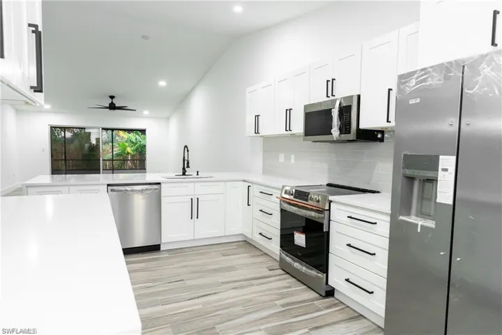 Kitchen with stainless steel appliances, vaulted ceiling, white cabinets, recessed lighting, and a ceiling fan