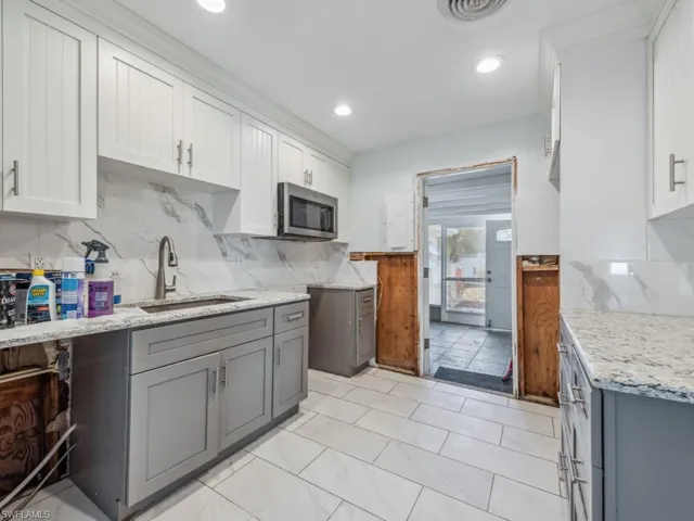 Kitchen with gray cabinets, sink, white cabinetry, and backsplash