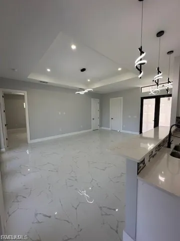 Kitchen featuring pendant lighting, a tray ceiling, light stone counters, light marble finish floors, and open floor plan
