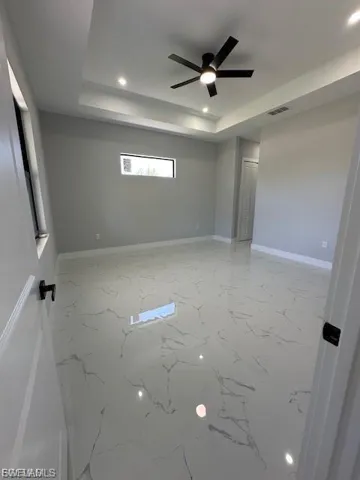Unfurnished room with recessed lighting, a ceiling fan, a raised ceiling, and light marble finish flooring