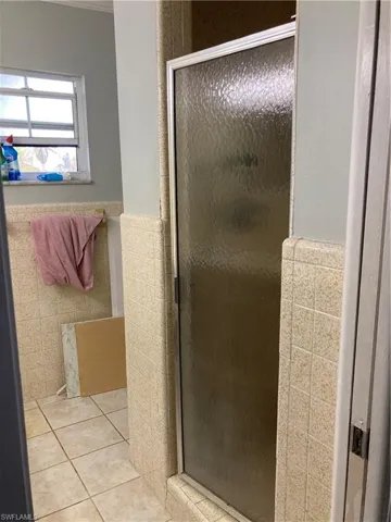 Bathroom with a shower with shower door, tile patterned flooring, and tile walls
