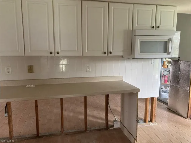 Kitchen with tasteful backsplash, light wood-type flooring, and white cabinetry