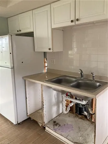 Kitchen featuring white cabinets, light wood-type flooring, decorative backsplash, and sink lower cabinets damaged