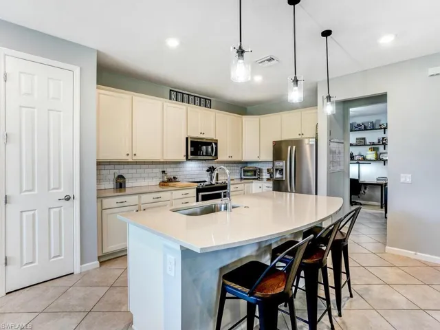 Kitchen featuring a breakfast bar, light tile patterned floors, pendant lighting, stainless steel appliances, and a center island with sink