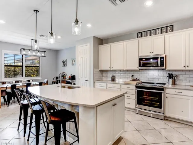Kitchen featuring a kitchen island with sink, sink, white cabinets, hanging light fixtures, and stainless steel appliances
