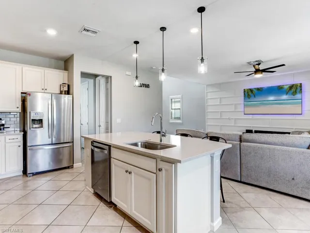 Kitchen featuring ceiling fan, an island with sink, sink, white cabinetry, and stainless steel appliances