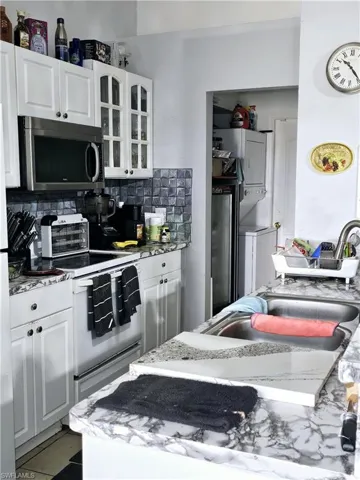 Kitchen with tile floors, white cabinets, backsplash, and range with electric cooktop