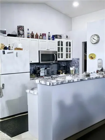 Kitchen featuring light stone countertops, tile flooring, tasteful backsplash, white fridge, and white cabinetry