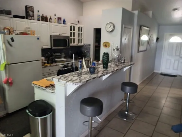 Kitchen featuring tasteful backsplash, tile floors, a kitchen bar, white cabinets, and appliances with stainless steel finishes