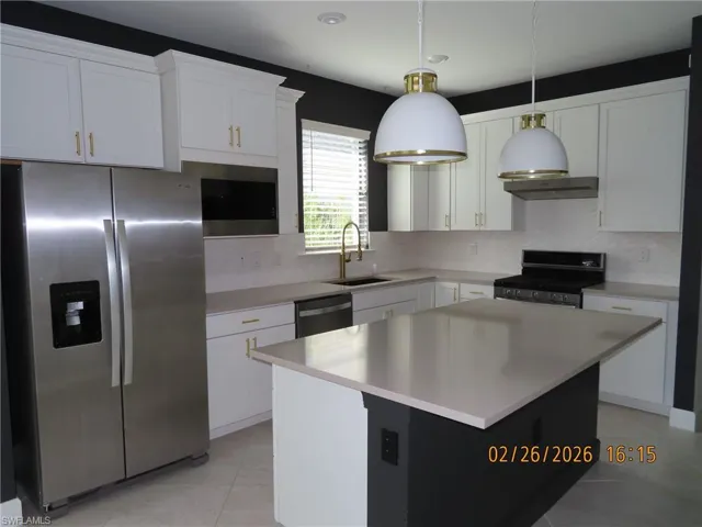 Kitchen with stainless steel appliances, white cabinets, decorative backsplash, and hanging light fixtures