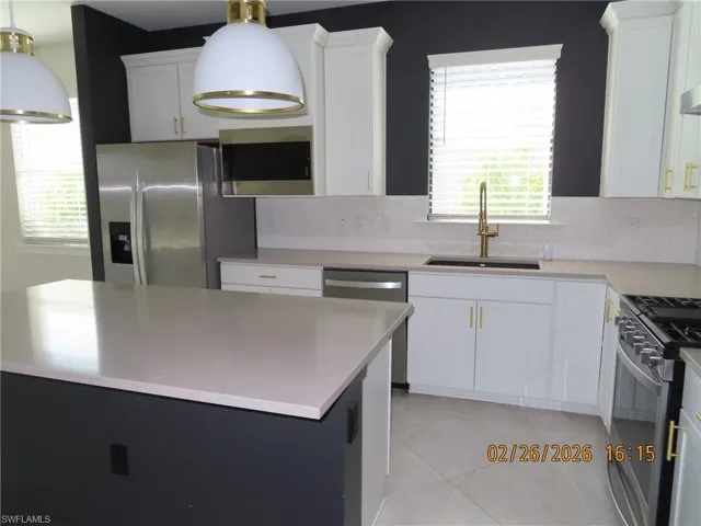 Kitchen with stainless steel appliances, white cabinets, decorative backsplash, and healthy amount of natural light