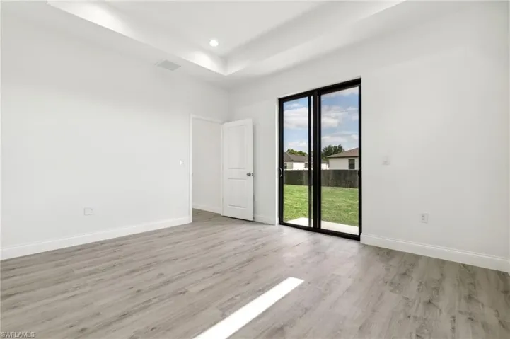 Unfurnished room featuring a tray ceiling, light wood-style floors, visible vents, and baseboards