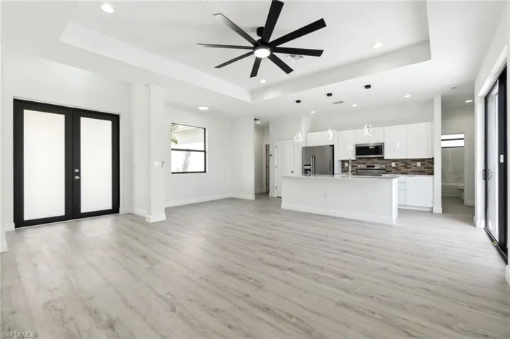 Unfurnished living room with french doors, a ceiling fan, a tray ceiling, light wood-type flooring, and recessed lighting