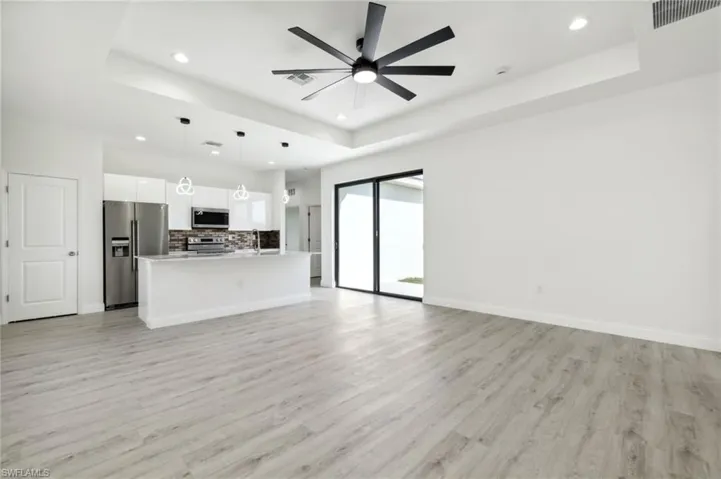 Unfurnished living room featuring a ceiling fan, recessed lighting, visible vents, a raised ceiling, and light wood-style floors