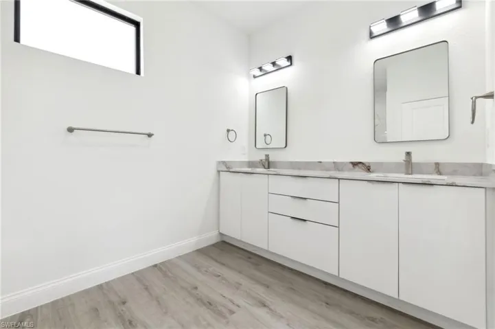 Bathroom featuring baseboards, double vanity, a sink, and wood finished floors