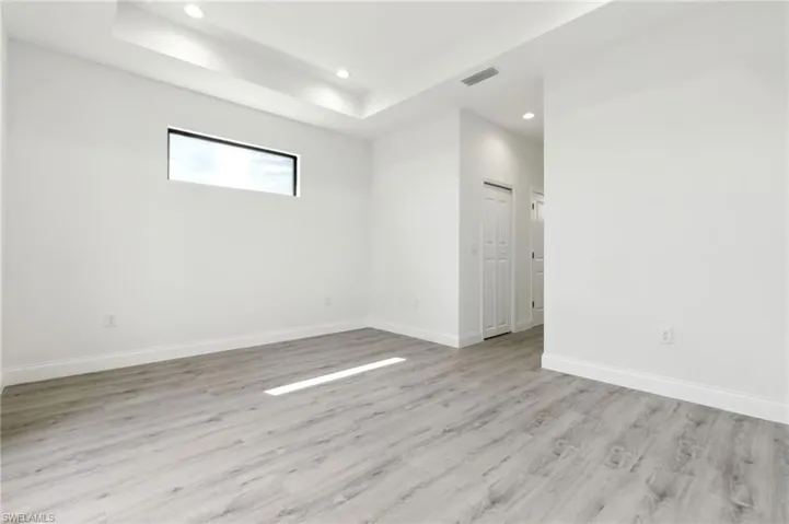Spare room with a tray ceiling, recessed lighting, baseboards, visible vents, and light wood-type flooring